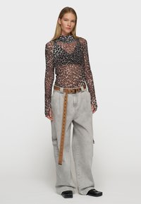 Durchsichtiger Netz-Body mit Schwarz- und Braun-Leopardenmuster, kombiniert mit hellgrauen Cargo-Hosen und einem braunen Gürtel. Glattes, figurnahes Design.