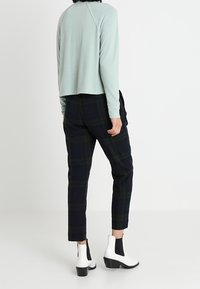 Lichtblauw, langemouwen top met een relaxte pasvorm, gecombineerd met donker geruite broek. Witte enkelboots met zwarte accenten en grove hakken.