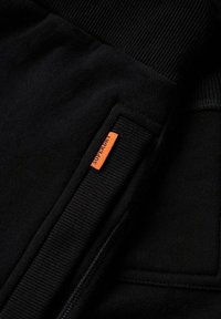 Zwarte katoen sweatshirt met geribbelde manchetten, met een oranje Superdry-label op de zak, een soepele textuur en een casual ontwerp.