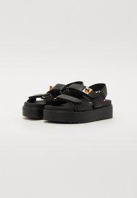 Black platform sandals with two wide straps and gold-tone hardware accents. The sole is textured for grip and features a thick, cushioned base.