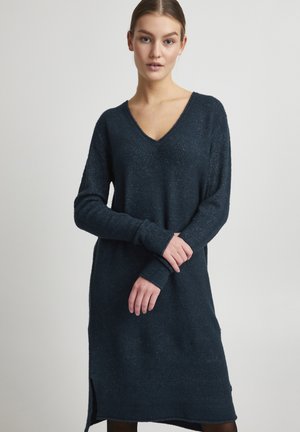 Lange mouwen, donkerblauwe trui jurk met een V-hals, geribde manchetten en zijsplitten. Zachte textuur met een licht gemêleerde afwerking.