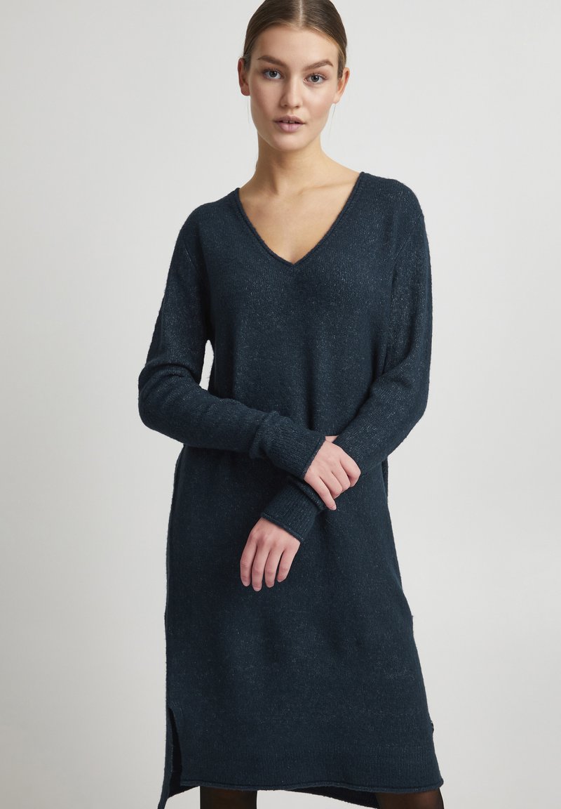 Robe pull à manches longues, bleu foncé, avec un décolleté en V, des poignets côtelés et des fentes latérales. Texture douce avec un fini légèrement chiné.