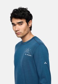 Langärmliges blaues Hemd aus weichem Stoff. Mit einem weißen Segelboot-Motiv auf der Brust und einem Logo auf dem Ärmel. Runder Halsausschnitt, gestickte Details.