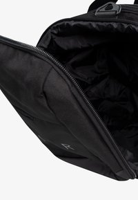 Mochila negra con un tejido robusto, cierre con cremallera y un interior espacioso. Presenta una textura suave y un detalle de logoMinimalista.
