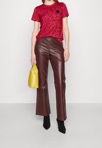 T-shirt imprimé léopard rose assorti à un pantalon évasé en cuir marron. Tenant un sac à main jaune. Des bottines noires complètent la tenue.