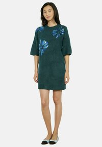 Teal trui-jurk met korte pofmouwen en bloemenpaillettenborduursel in blauw. Zachte textuur en ontwerp tot op de knie.