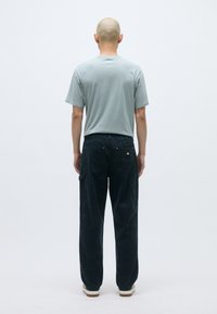 Ανοιχτό γκρι κοντομάνικο πουκάμισο, σκούρο ναυτικό παντελόνι με φαρδιές γραμμές, λεία υφή, ορατά ράψιμα και μπεζ αθλητικά παπούτσια. Πίσω όψη σε απλό φόντο.