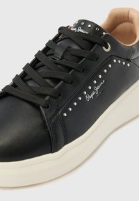 Čierne kožené tenisky s plochými čiernymi šnúrkami, striebornými cvokmi na boku a bielou gumovou podrážkou. Na boku je logo "Pepe Jeans".