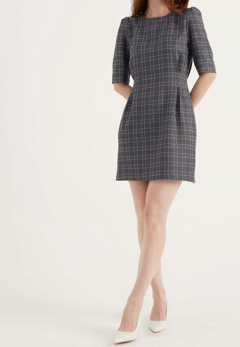 Robe à carreaux grise à manches courtes, silhouette ajustée et poches latérales. Fabriquée dans un tissu texturé, elle présente un col rond et une longueur au-dessus du genou.