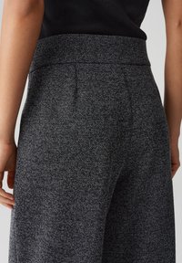 Graue strukturierte, hoch geschnittene Hose mit einem subtilen gepunkteten Muster und einem glatten Bund, von hinten gezeigt, wobei Taschen und Nähte hervorgehoben werden.