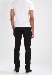 Black denim jeans with a slim fit, styled with a white short-sleeve t-shirt and black sneakers. Smooth texture and minimal detailing.
