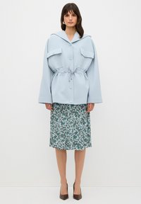 Chaqueta oversize de color azul claro con dos bolsillos en el pecho y cintura con cordón, combinada con una falda midi de estampado floral en tonos verdes y blancos.