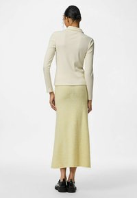 Romige geribde top met lange mouwen, gecombineerd met een pastelgele rok, die een gladde textuur en een rechte silhouet heeft, aangevuld met zwarte schoenen.