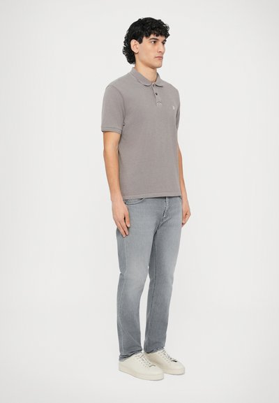 Γκρι πόλο μπλούζα με γιακά και τρία κουμπιά, συνδυασμένη με ανοιχτό γκρι τζιν και λευκά αθλητικά παπούτσια. Ομαλή υφή και casual σχεδιασμός.