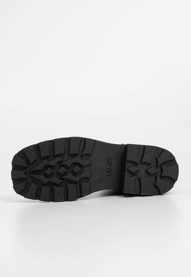 Czarna gumowa podeszwa buta z głębokimi bieżnikami i wzorzystym wzorem. Charakteryzuje się gładką fakturą i wzmocnionym brzegiem przy pięcie.