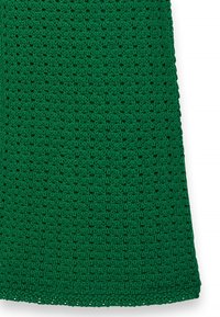 Adīta zaļa auduma ar atvērtu austu un teksturētu rakstu, ar viļņotiem maliņām. Materiāls izskatās mīksts un viegls.