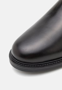 Black leather boot with a rounded toe, smooth texture, and a contrasting stitched sole. Smooth finish with a slight shine.