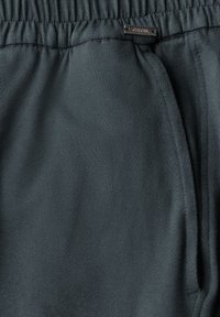 Pantalons de survêtement vert foncé avec une taille élastique, dotés de poches latérales et d'une texture lisse. Petite étiquette de marque près de la taille.