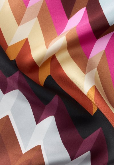 Gros plan d’un tissu avec une texture pliée présentant un motif zigzag coloré dans des tons rose, marron, orange, crème, noir et blanc.