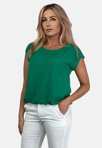 Zielony krótki rękaw top wykonany z lekkiego materiału, z okrągłym dekoltem i luźnym krojem, zestawiony z białymi spodniami.