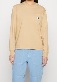 Beige långärmad skjorta i bomull, med en bröstficka som har en logotags. Skjortan har en avslappnad passform och ribbade manschetter.