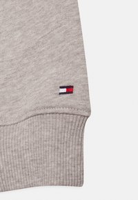 Cuff di felpa grigia lavorata a maglia con texture a coste. Presenta una piccola toppa ricamata multicolore in rosso, bianco e blu.