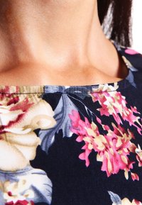 Látka s květinovým vzorem na tmavě námořnickém pozadí; obsahuje růžové a krémové květy; kulatý výstřih s viditelným švem.