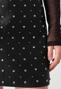 Svart kjole med en tettsittende design, pyntet med varierte størrelser av klare rhinestones og en mesh-sleeve med røde hjerter. 