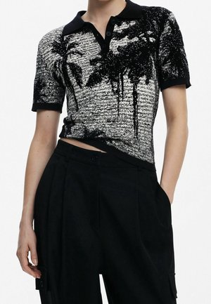 Persoon draagt een zwart-wit gebreide polo met korte mouwen met palmboom patroon en zwarte hoge taille broek met zakken.