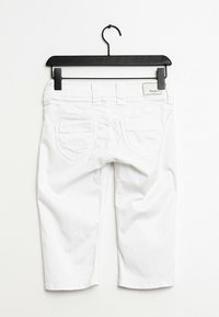 Pantalones capri blancos de algodón, con un diseño clásico de cinco bolsillos y una etiqueta en el bolsillo trasero. Colgados de una percha negra.