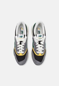 Šedé a černé tenisky s zelenými a žlutými akcenty, s vrchním materiálem z prodyšné síťoviny a bílými tkaničkami. Výrazné logo na jazyku.