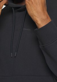 Námořnická modrá mikina s kapucí z měkkého materiálu, s tkaničkami, přední kapsou a jemně embosovaným logem na hrudi.