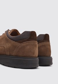 Chaussures en daim marron avec un panneau texturé marron foncé au niveau du talon et une semelle en caoutchouc noire, présentant un design à profil bas et des accents cousus.