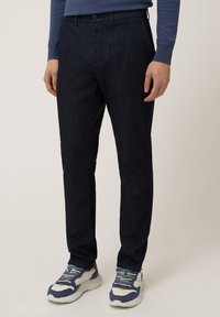 Pantalones oscuros de tejido texturizado, con una silueta ajustada, bolsillos laterales y un cierre de botón en la cintura.