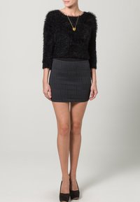 Pull noir en peluche, coupe courte, avec des manches trois-quarts, associé à une mini-jupe noire ajustée et texturée. Des chaussures noires à talons hauts complètent le look.