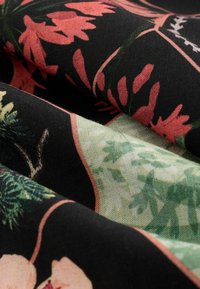 Tessuto floreale con sfondo nero caratterizzato da motivi botanici in rosa e verde, che mette in mostra diverse trame e ricchi contrasti di colore.
