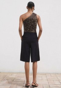 Top asimmetrico a stampa leopardata marrone abbinato a pantaloni shorts neri fino al ginocchio, in tessuto liscio e con una vestibilità comoda. Sandali con fasce sottili.