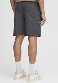 Grå sweatshorts med elastisk talje, baglomme og en afslappet pasform, kombineret med hvide sportsstrømper og beige sneakers.