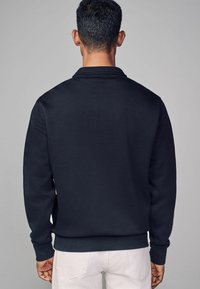 Maritieme sweatshirt met lange mouwen, ribgebreide manchetten en zoom, en een vlakke kraag. Zachte textuur van de stof, achterkant zichtbaar, minimaal detail.