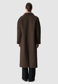 Bruine wollen jas met een brede kraag, lange mouwen en een relaxte pasvorm. Ontworpen om onder de knie te vallen, met minimale stiksels.