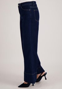 Donkerblauwe denim wijde pijpen jeans met een hoge taille, voorzien van opvallende stiksels en een ontspannen pasvorm. Met een opvallend afgewerkte wijde zoom.