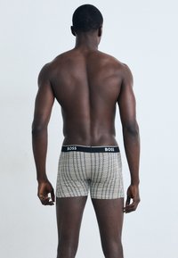 Boxer Shorts in Schwarz, Weiß und Goldmuster. Hergestellt aus elastischem Material, mit einem schwarzen Bund, der mit dem 'BOSS'-Logo versehen ist. Kurze Beine und körpernahe Passform.