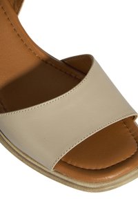 Beige leren sandaal met een brede teenband en een tan voetbed. Plat zool met zichtbare stiksels op de band.