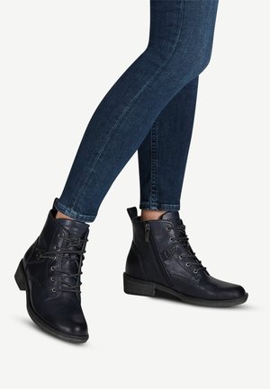 Botas de cuero negras hasta el tobillo con cordones en la parte delantera, cremallera lateral y tacón cuadrado, combinadas con jeans ajustados azul oscuro.