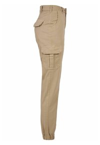 Pantalon cargo beige avec jambe fuselée, ourlet élastique à la cheville, poches latérales et poche à rabat sur la cuisse. Fabriqué en tissu résistant.