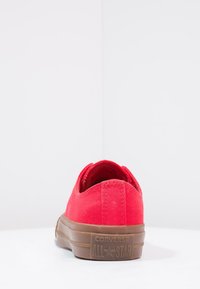 Baskets en toile rouges avec semelle en caoutchouc marron, design bas, bout arrondi et détails cousus. Présente la marque Converse All Star sur le talon.