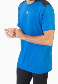 Camiseta deportiva azul de manga corta, con textura suave, acentos negros en los hombros y un pequeño logo de una araña en el pecho.