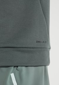 Gros plan sur un vêtement de sport vert montrant le texte "DRI-FIT" près de l'ourlet au-dessus d'un short vert assorti avec une étiquette blanche.