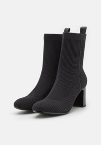 Schwarze, gerippte Knöchelstiefel aus dehnbarem Material, mit spitzem Zehenbereich und stabiler, dicker schwarzer Ferse. Minimalistisches Design ohne Verzierungen.