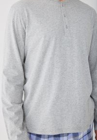 Sivá dlhá rukávová henley košeľa vyrobená z mäkkej tkaniny, s trojcovou gombíkovou légou a hladkou štruktúrou, v kombinácii s modrými károvanými nohavicami.